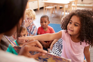 Little girl pointing at book during story time at nursery